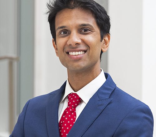Smiling Ravi Parikh in a red tie, white shirt and blue jacket. and blue