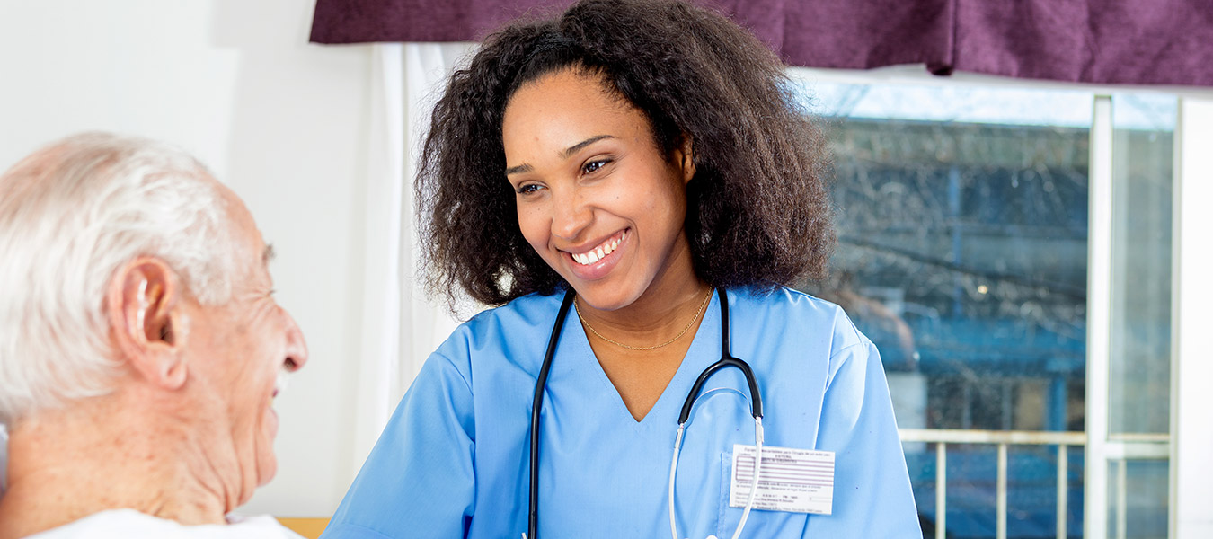 Caregiving nurse happy with elder patient in nursing home.