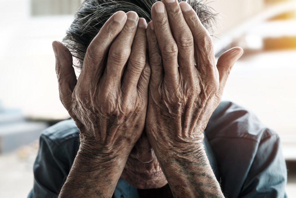 An elderly person with their hands on their face.