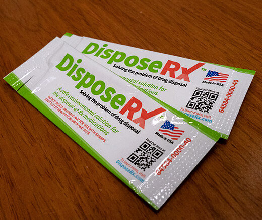 two white packets with green and red writing that says DisposeRX on a wood surface.