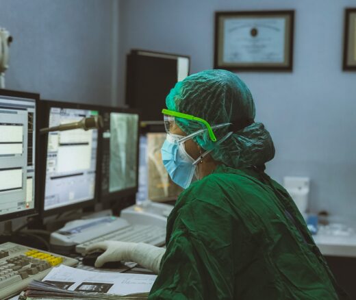 A clinician in PPE looks at information on a computer monitor.